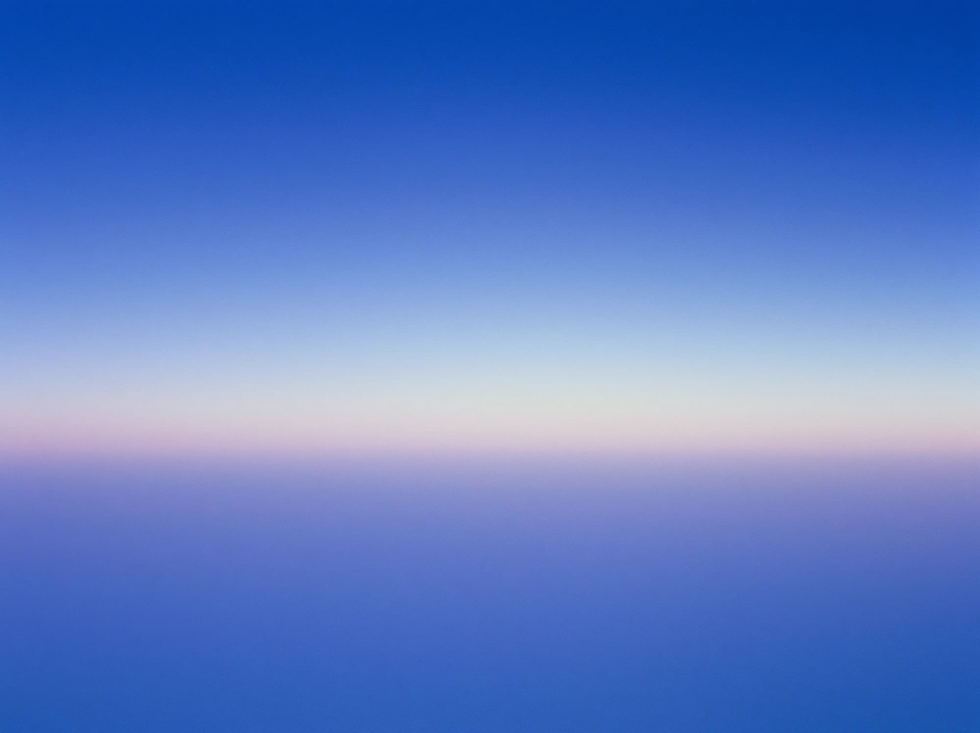 A smooth blue gradient with a thin band of pale pink light along the horizon.