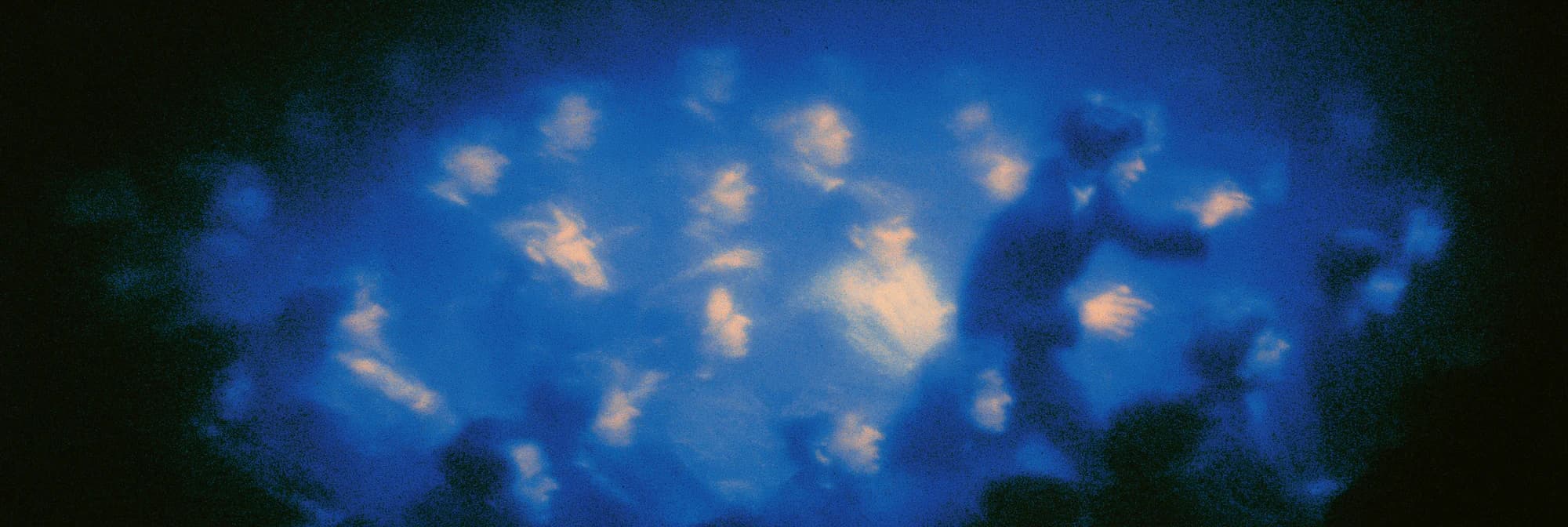 A blurred crowd of faces in deep blue light, lit warm from below, with one figure in motion on the right.