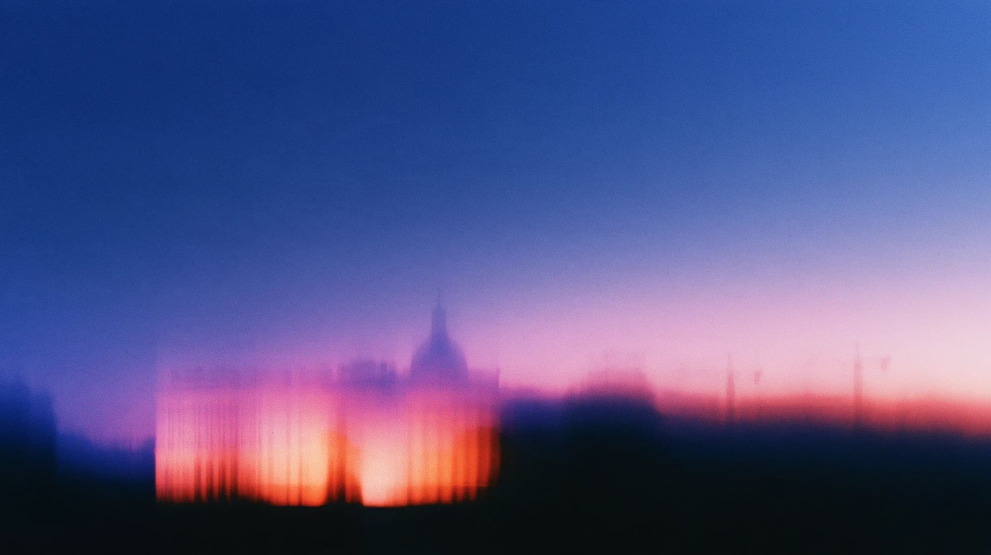 The blurred silhouette of a grand building beneath a blue and pink dawn sky, with faint construction cranes to the right.