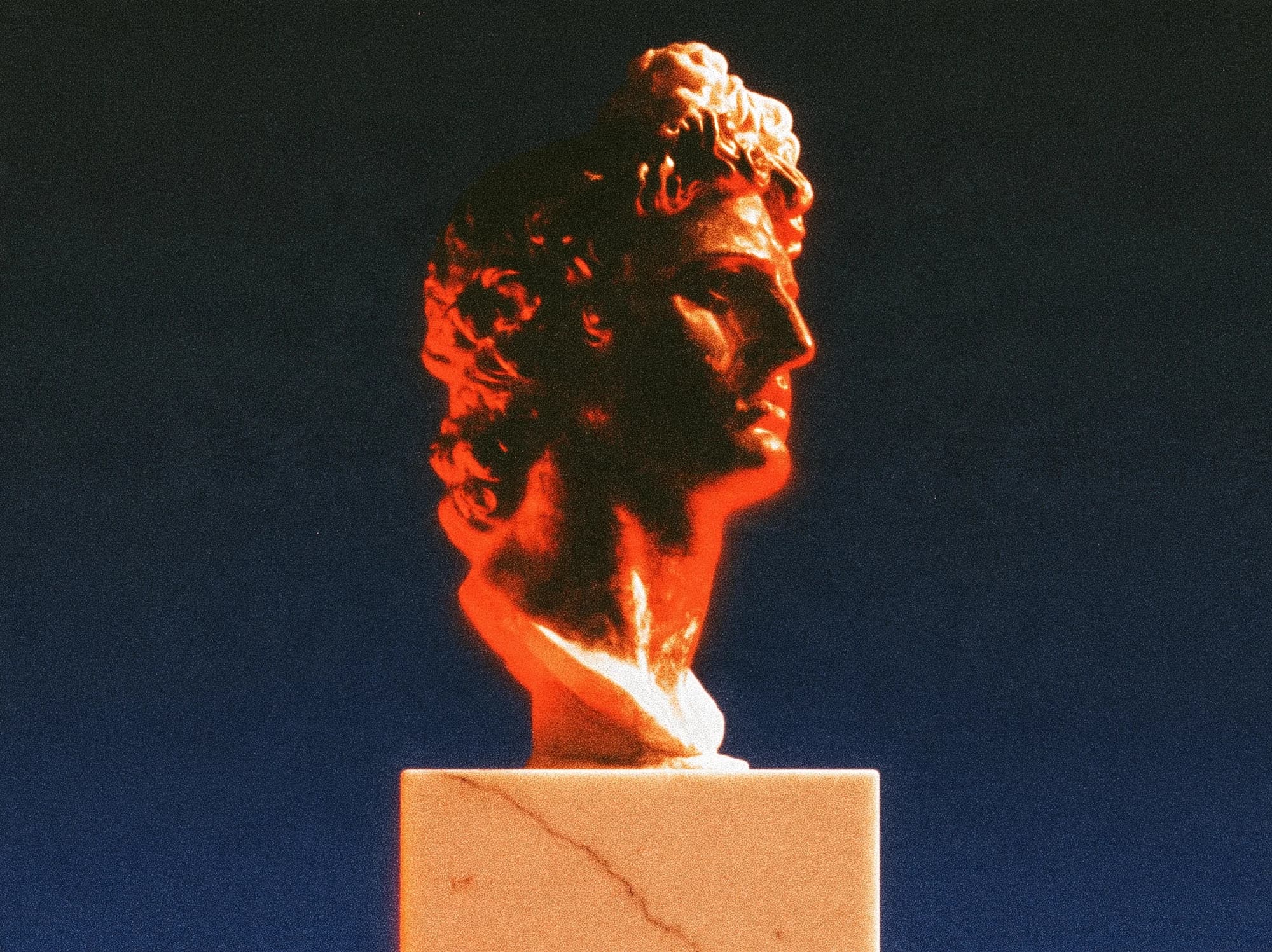 A marble bust lit in red on a cracked pedestal against a dark blue background.