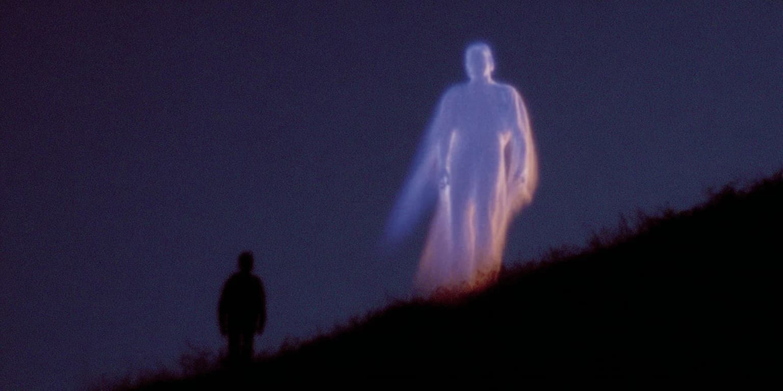 A small dark figure stands on a hillside at dusk below a towering, translucent glowing figure in a long robe.