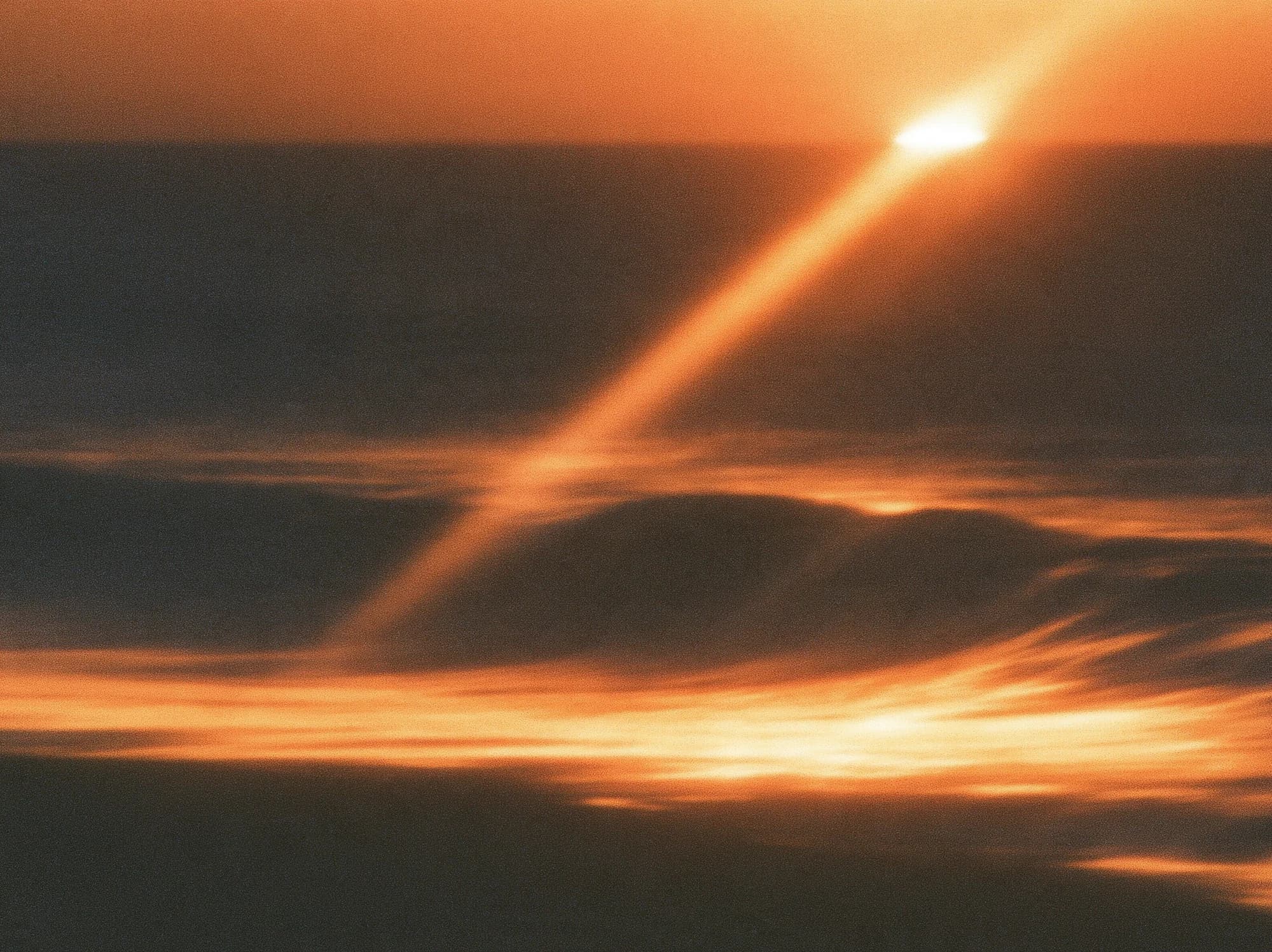 Amber sunlight falls across a dark shoreline and blurred waves.